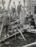 600359 Afbeelding van enkele werknemers bij een waterpomp tijdens de werkzaamheden voor de bouw van een materieelloods ...